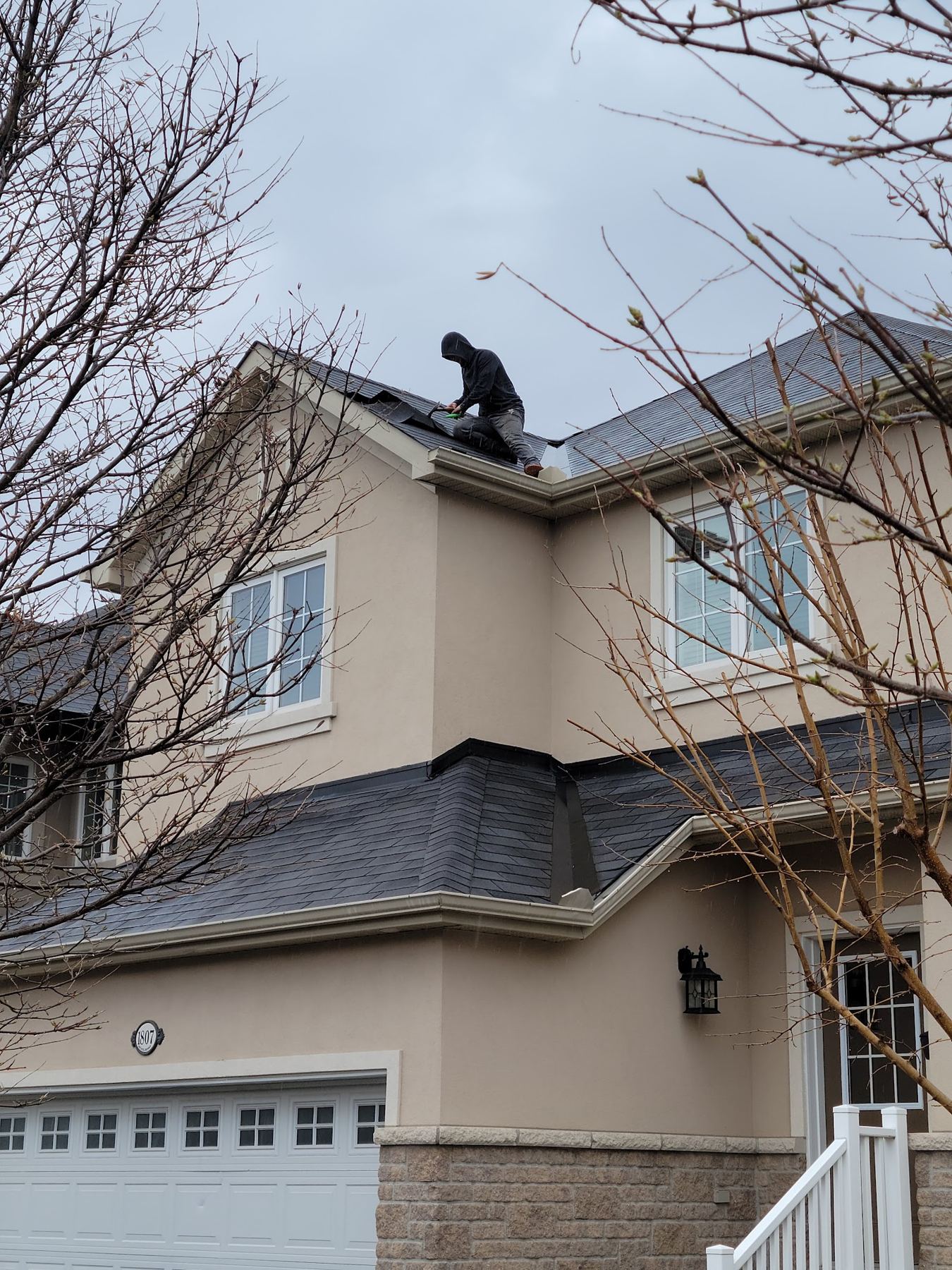 A roofer working on the shingle roof of a stucco house