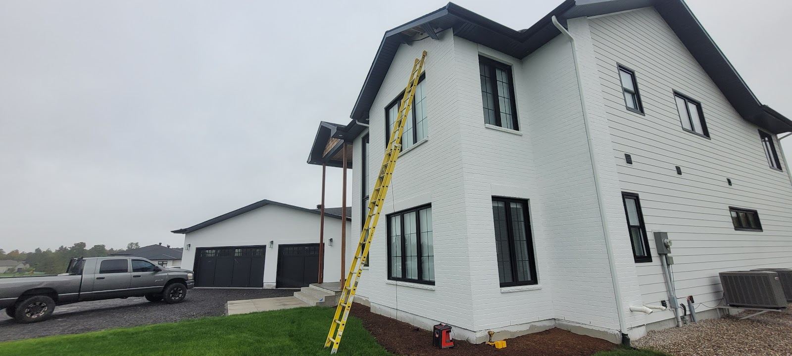 White siding on a new two-storey house, with a ladder and a pickup truck